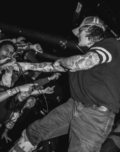 A black and white photo of a man with tattoos performing in front of a crowd at a Los Angeles music venue.