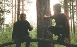 Two men sitting on a log in the woods.