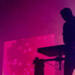 A silhouette of a person standing on a keyboard in front of a purple light.