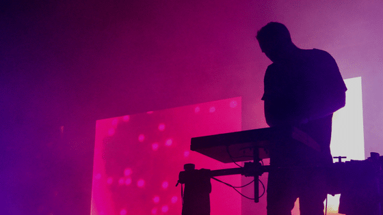 A silhouette of a person standing on a keyboard in front of a purple light.