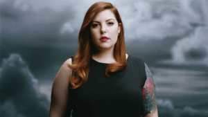 A woman with tattoos standing in front of a cloudy sky.