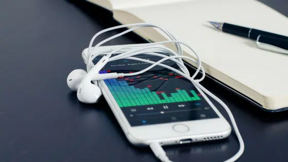 An iphone with earphones next to a notebook and pen.