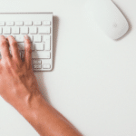A woman's hands typing on a white keyboard.