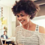 A woman is smiling while using a laptop in a coffee shop.