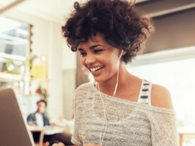 A woman is smiling while using a laptop in a coffee shop.