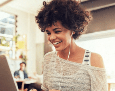 A woman is smiling while using a laptop in a coffee shop.