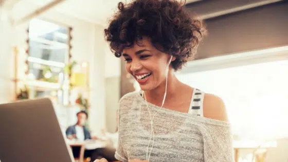 A woman is smiling while using a laptop in a coffee shop.