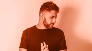 A man with a beard standing in front of an orange wall.