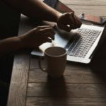 A man using a laptop on a wooden table.