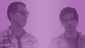 Two men standing in front of a purple background.