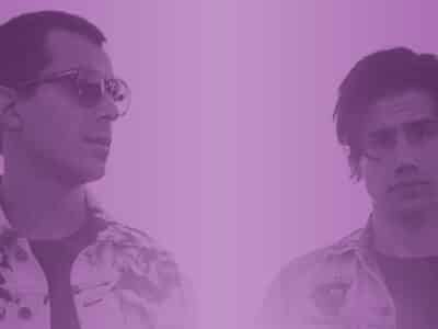 Two men standing in front of a purple background.