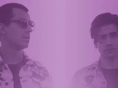 Two men standing in front of a purple background.