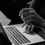 A black and white photo of a person using a laptop.