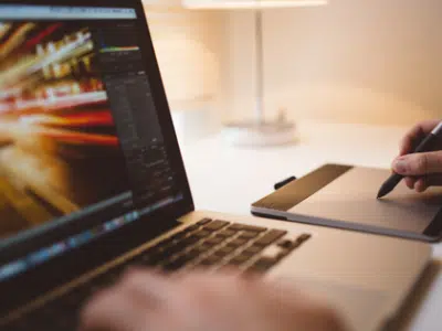 A person writing on a laptop with a pen.