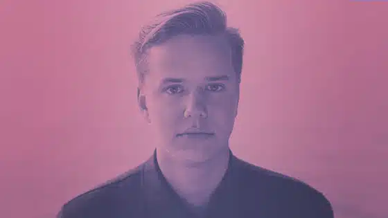 A man is standing in front of a pink background.