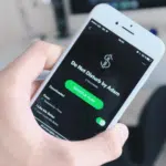 A person holding up a phone with the spotify app on it.