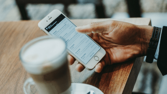 A hand holding a smartphone next to a cup of coffee.