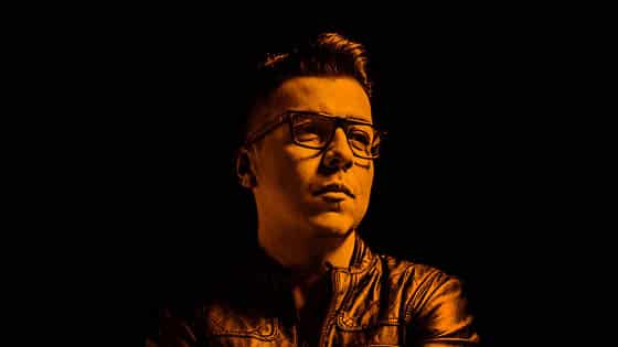 A man in glasses is standing in front of a black background.