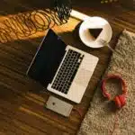 A laptop, headphones, and a cup of coffee on a wooden floor.