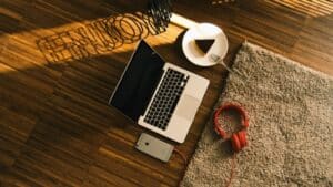 A laptop, headphones, and a cup of coffee on a wooden floor.