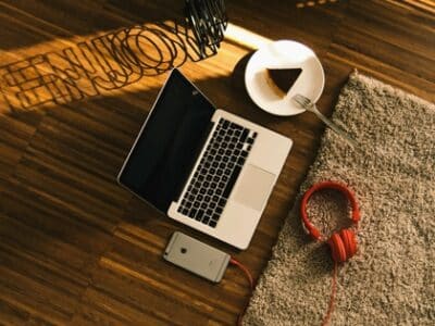 A laptop, headphones, and a cup of coffee on a wooden floor.