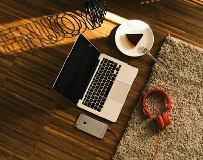 A laptop, headphones, and a cup of coffee on a wooden floor.