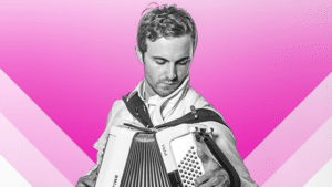 A man holding an accordion in front of a pink background.