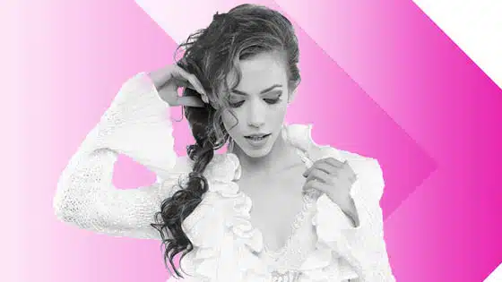 A woman is posing in front of a pink and white background.