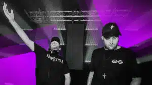Two men in black shirts standing in front of a purple background.
