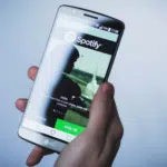 A person holding up a smartphone with the spotify app on it.