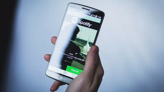 A person holding up a smartphone with the spotify app on it.