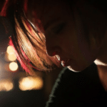A woman with red hair holding a microphone in the dark.