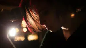 A woman with red hair holding a microphone in the dark.