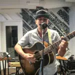 A man playing an acoustic guitar in front of a microphone.