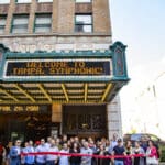 A group of people cutting a ribbon in front of a theater.