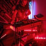 A man playing a keyboard in a room with red lights.