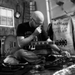 A bald man sitting on the floor with a guitar.