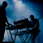 Two people standing in front of a keyboard.