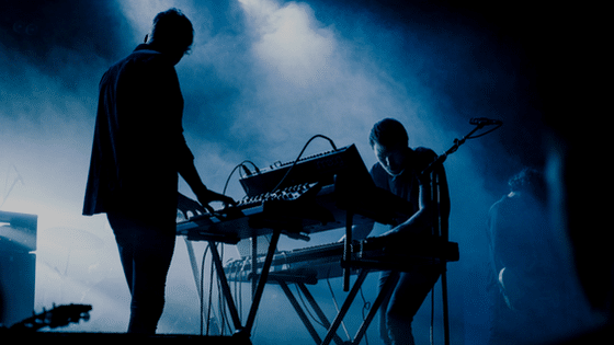 Two people standing in front of a keyboard.