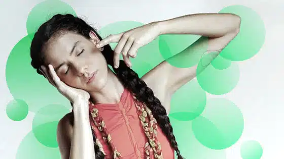 A woman with braided hair posing in front of a green background.