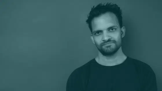 A man with a beard standing in front of a green wall.