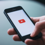 A person holding a cell phone with a youtube button on it.