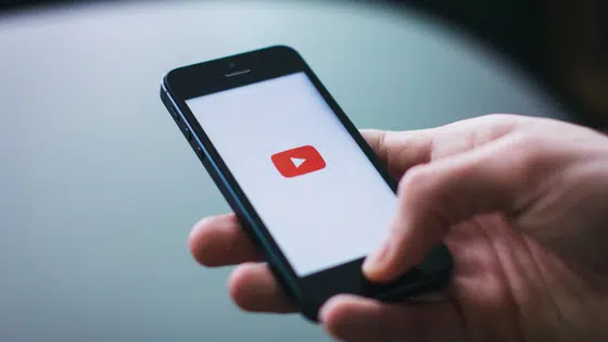 A person holding a cell phone with a youtube button on it.