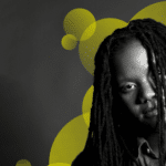 A man with dreadlocks in front of a yellow background.