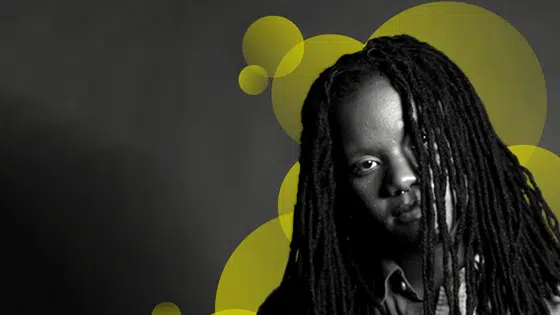 A man with dreadlocks in front of a yellow background.