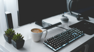 A desk with a computer, keyboard and cup of coffee.