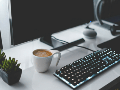 A desk with a computer, keyboard and cup of coffee.