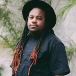A man with dreadlocks wearing a black shirt and hat.
