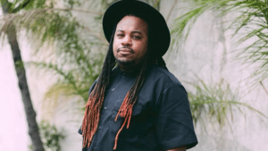 A man with dreadlocks wearing a black shirt and hat.
