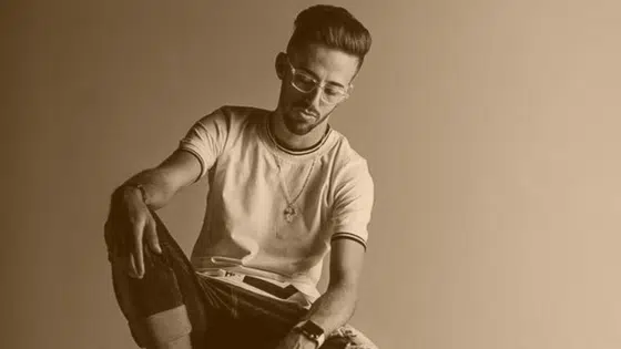 A man sitting on a stool with his hands on his knees.